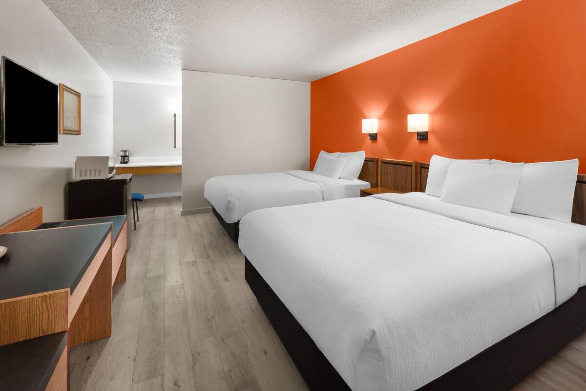 A hotel room with two beds, a desk, a chair, a TV, and a coffee machine.