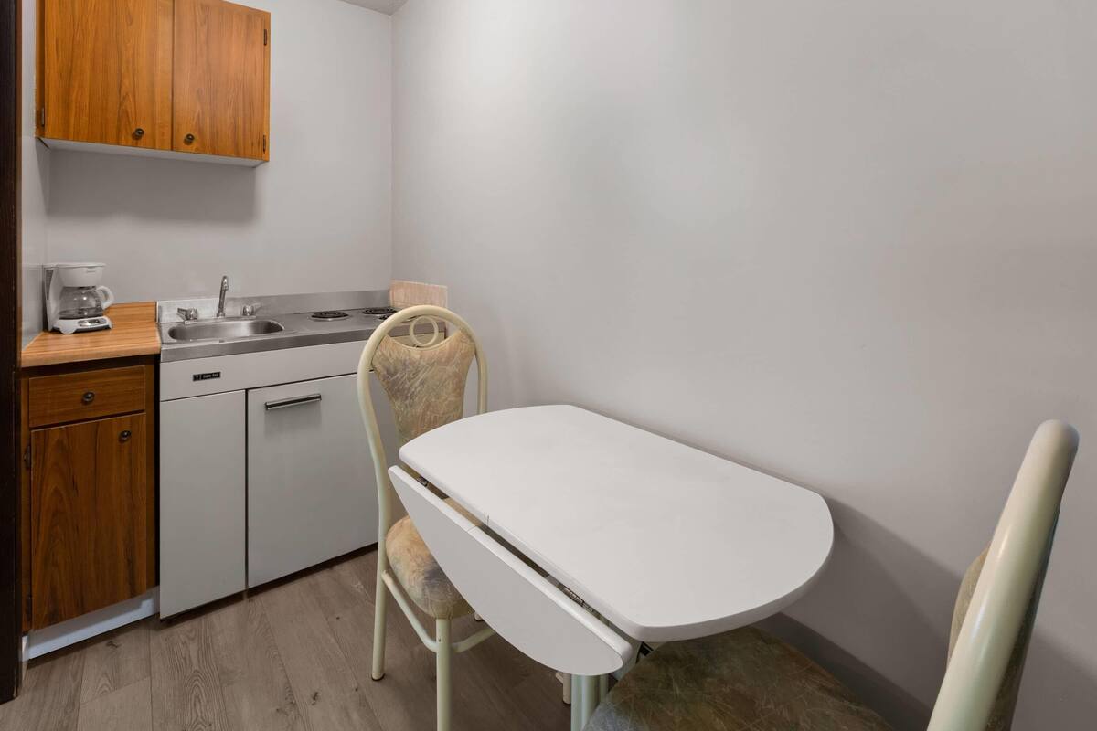A compact kitchen with a sink, stove, and a small dining table with a chair.