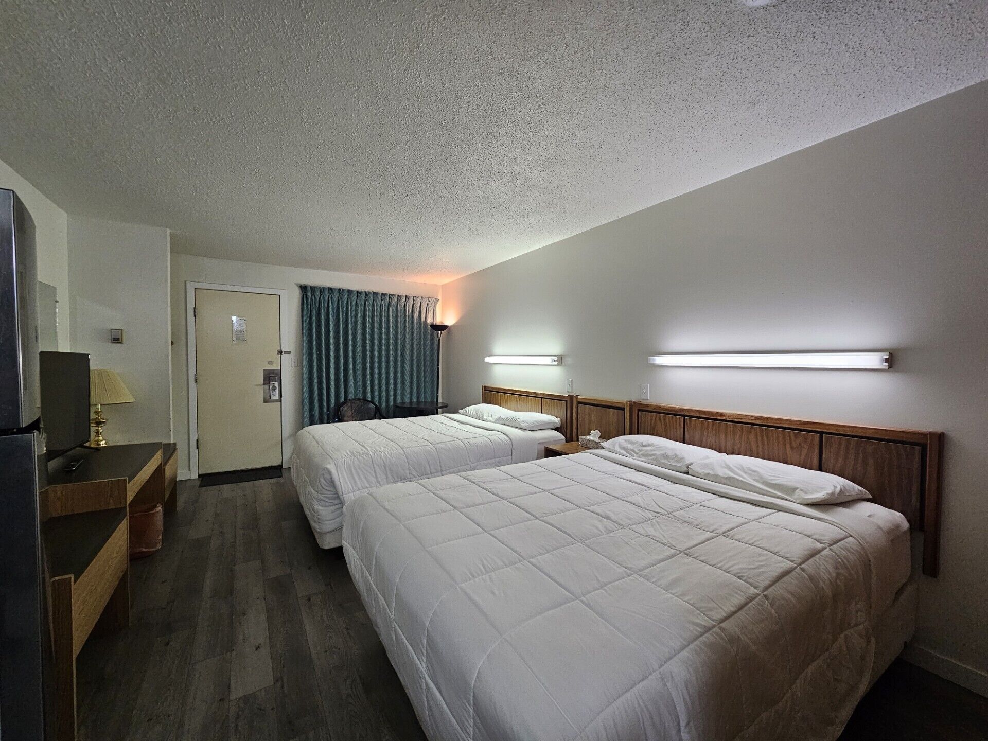 A hotel room with two beds, a desk with a lamp, a TV, and a door.