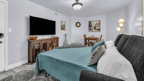 Une chambre à coucher comprenant un lit, une télévision, un ventilateur de plafond, une table à manger avec des chaises et une lampe.