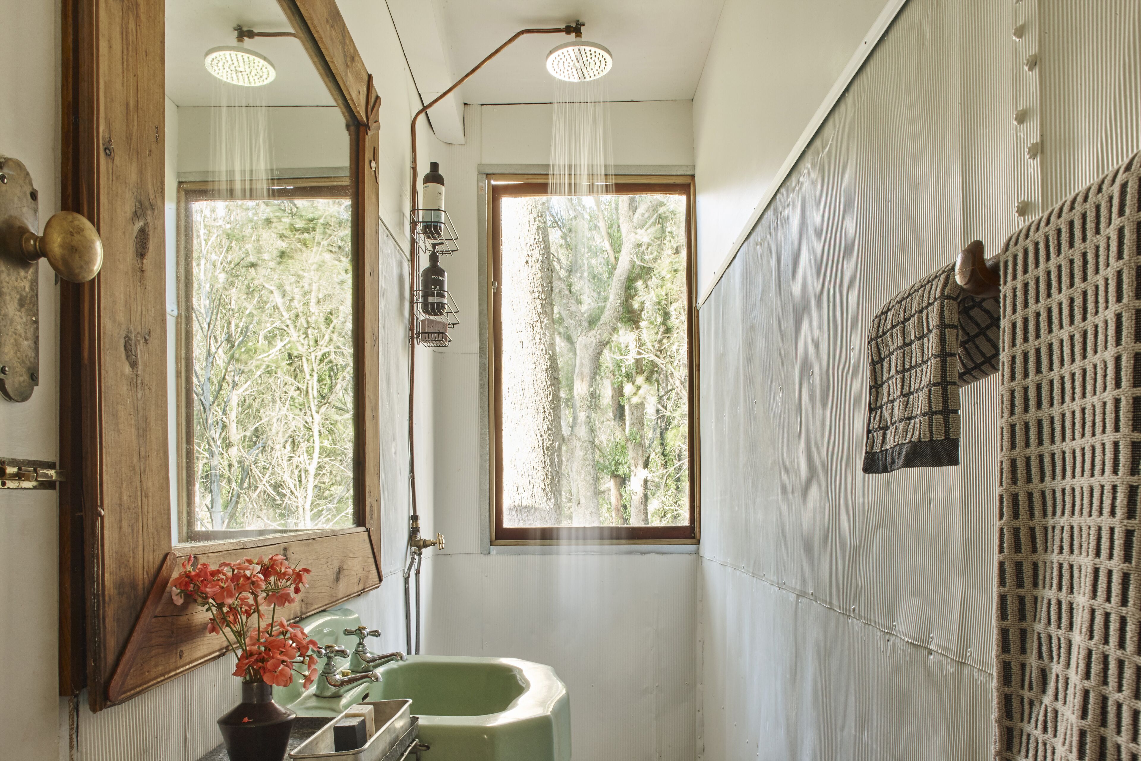 Een badkamer met een groene wastafel, een spiegel en een douche. Er is een raam dat natuurlijk licht en uitzicht op bomen biedt.