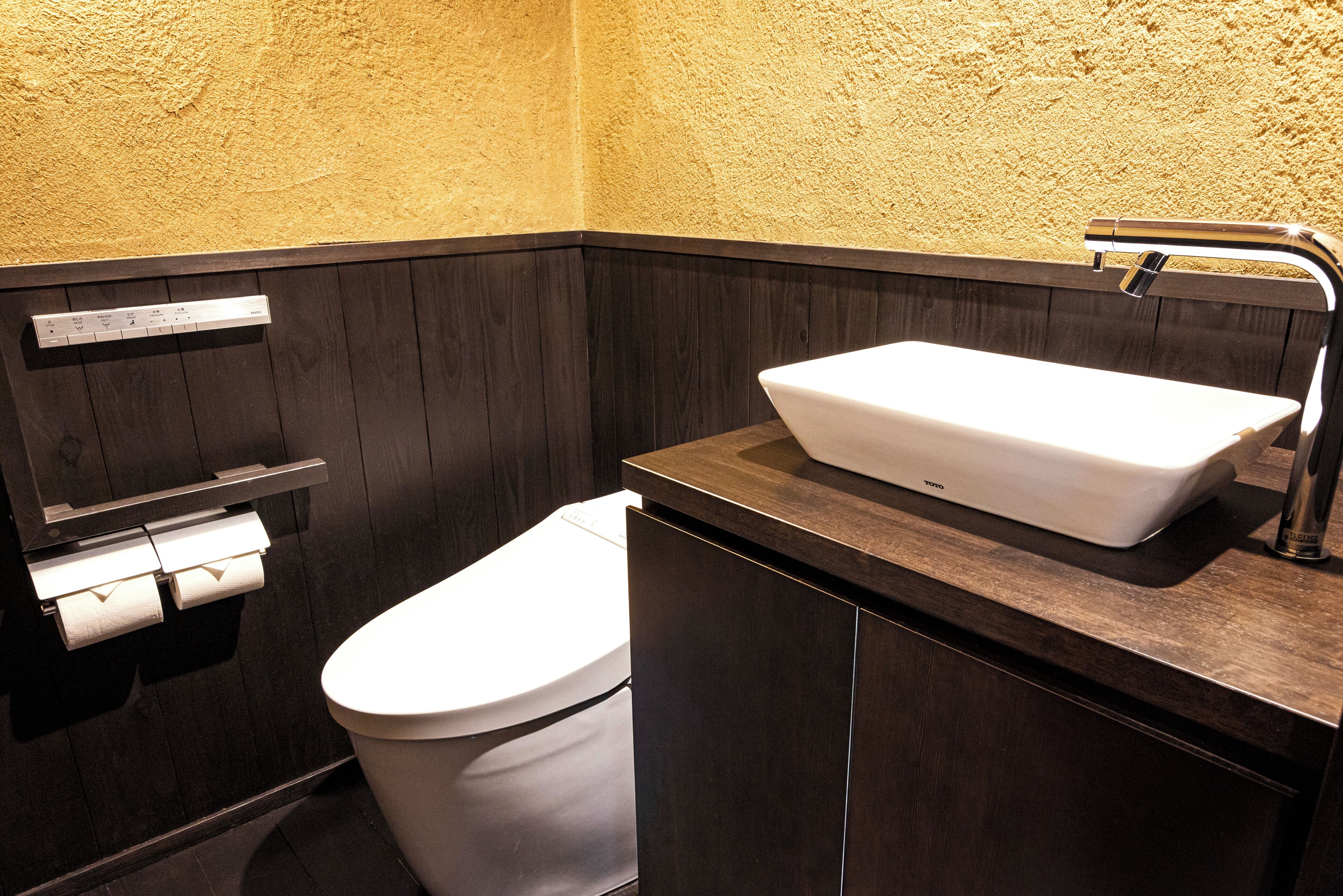 A modern bathroom with a white toilet, a built-in sink with a chrome faucet, and a wooden vanity.