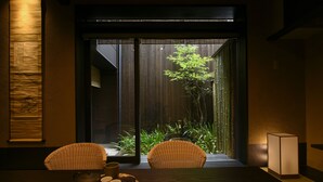 Ein traditioneller japanischer Raum mit Tatami-Böden, einem niedrigen Tisch mit Tee-Service und Blick auf einen Bambusgarten durch eine Schiebetür.