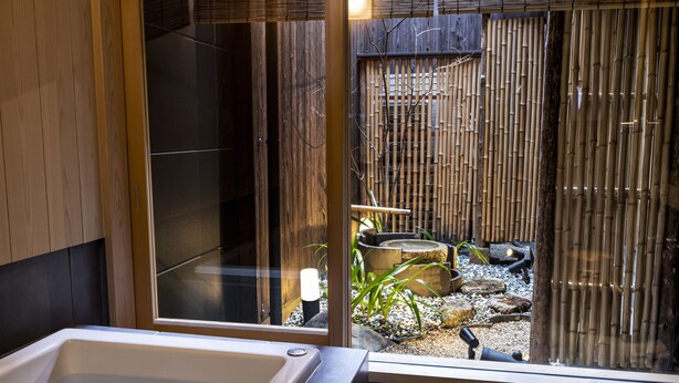 Ein modernes Badezimmer mit einer großen Badewanne, einer gläsernen Duschkabine und Blick auf einen Bambusgarten.