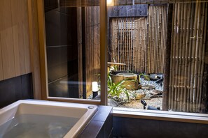 A modern bathroom with a large bathtub, a glass-enclosed shower area, and a view of a bamboo garden. - Rinn Premium Hiun (Kyoto)