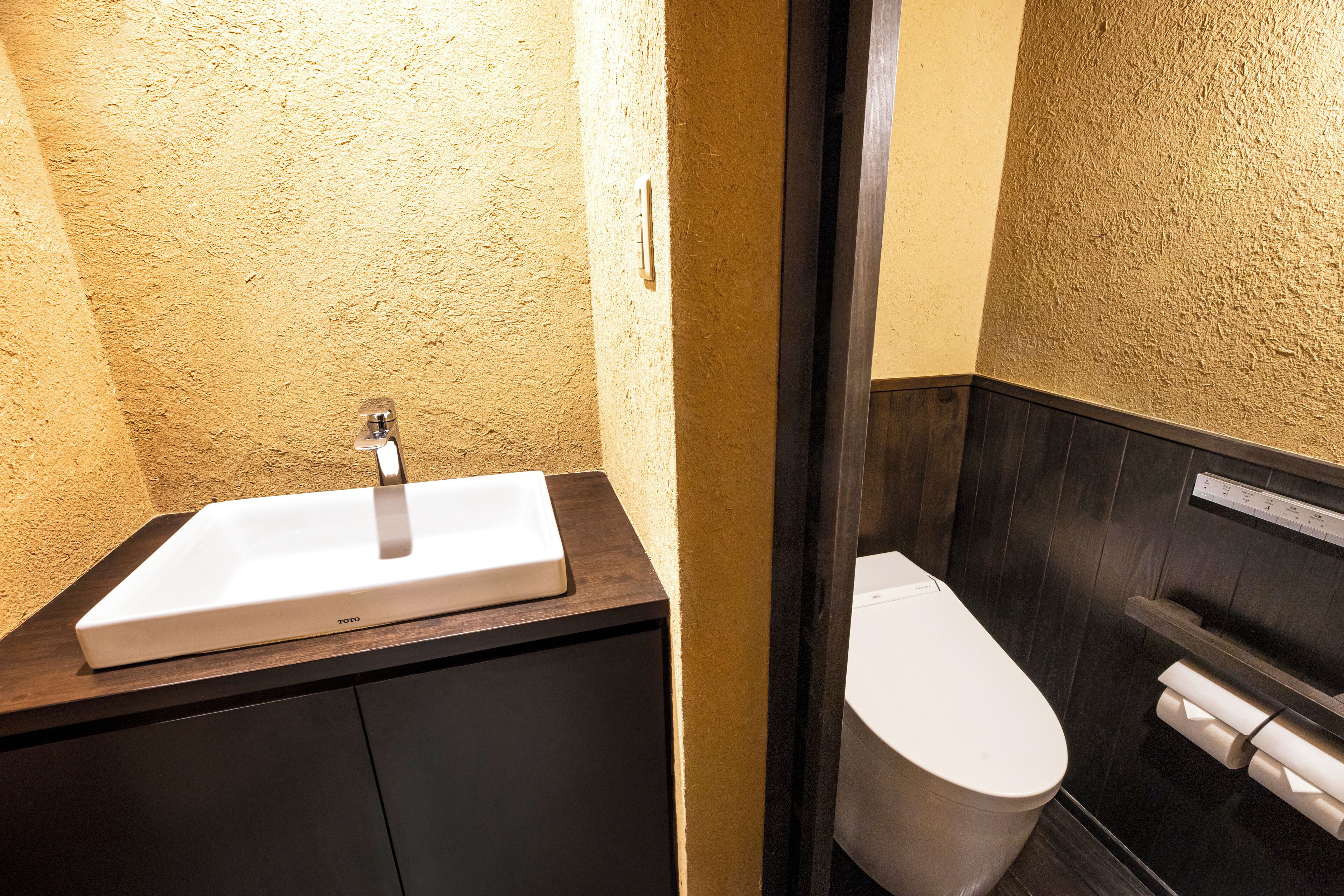 Une salle de bain avec un lavabo blanc, un meuble en bois foncé et des toilettes blanches.