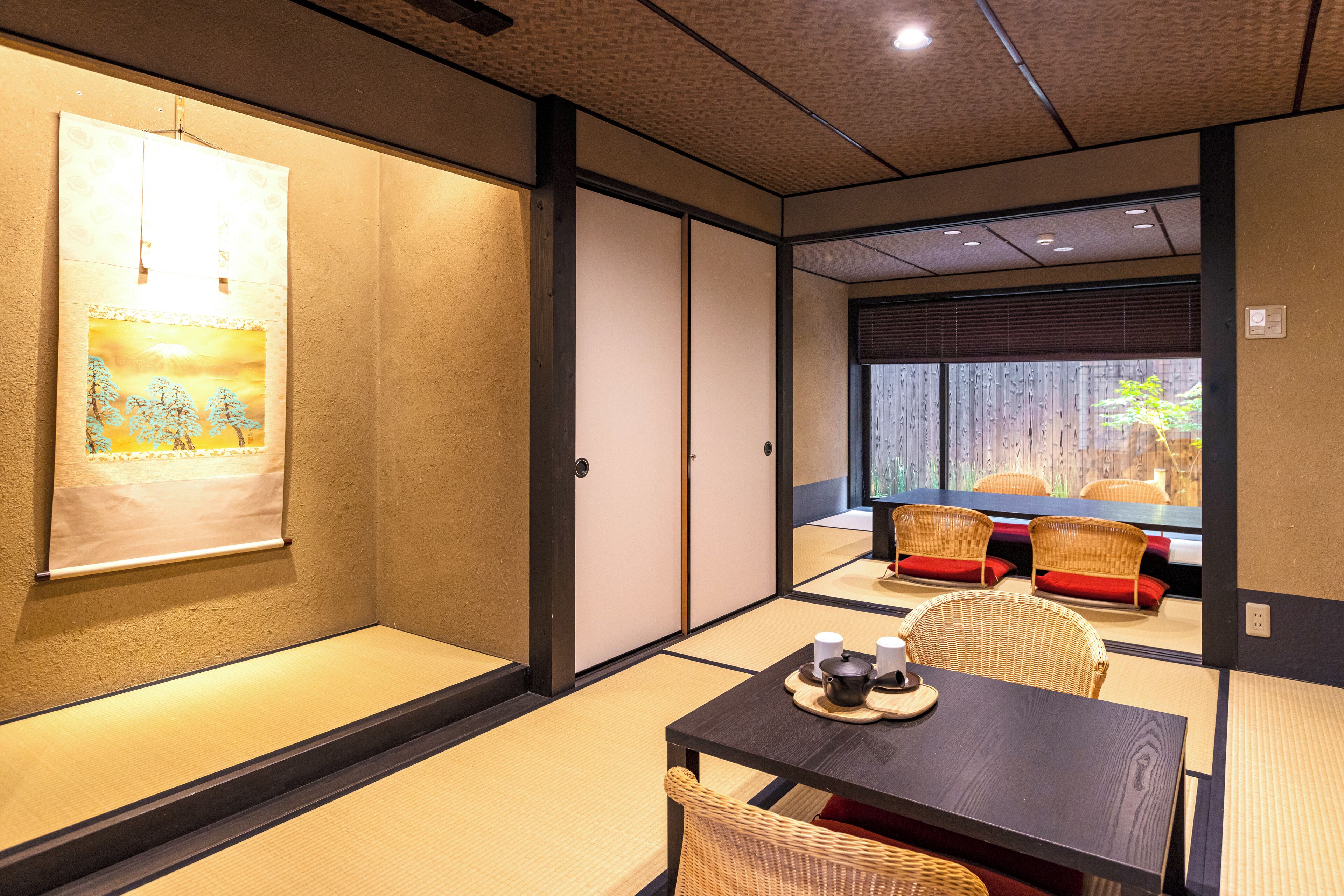Una habitación japonesa tradicional con suelo de tatami, una mesa baja con tapa de madera oscura y una silla trenzada.