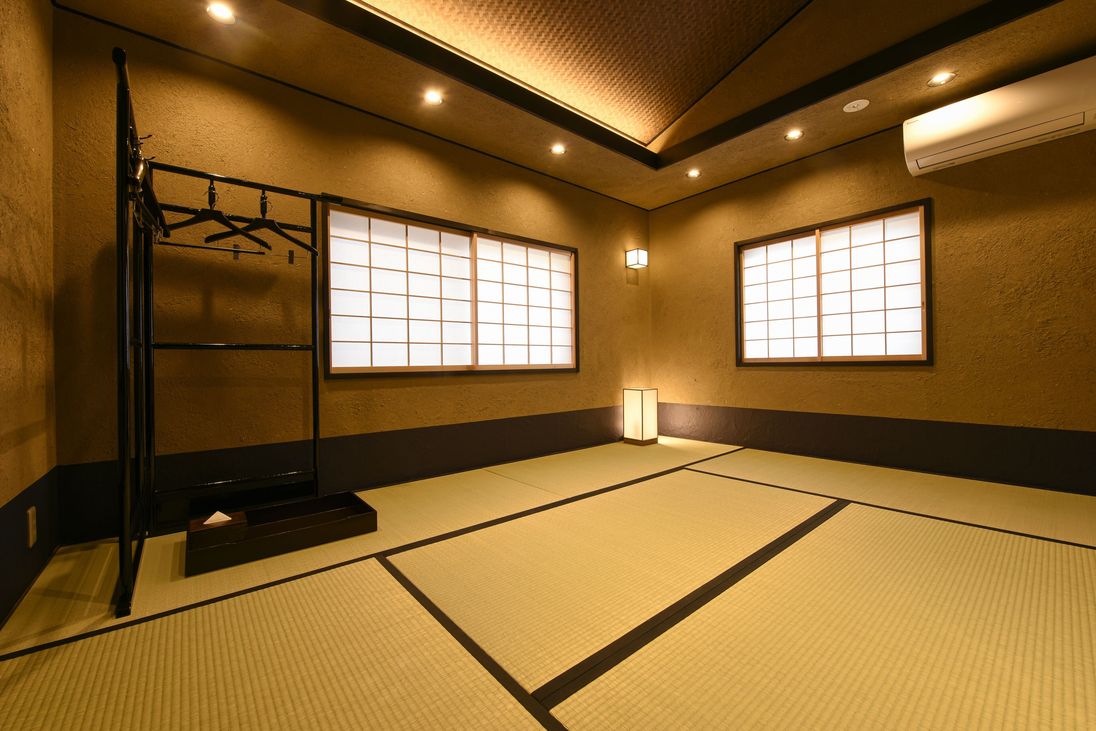 Een kamer met tatami matten, schuifdeuren, een hangende kapstok en een wandairconditioning.
