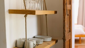 Une étagère en bois, ornée de verres et d’assiettes, est adossée à un mur.