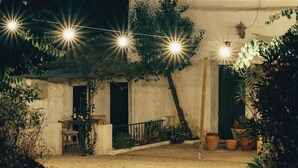 Un bâtiment avec un toit en tuiles, un petit patio avec une table et des chaises, et des guirlandes lumineuses.