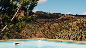 Une piscine offrant une vue dégagée sur un pin et un paysage vallonné en arrière-plan.
