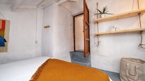 Ein Schlafzimmer mit einem Bett, einer Holztür, einer kleinen Treppe, einem Regal mit einer Pflanze und einer Tasche.