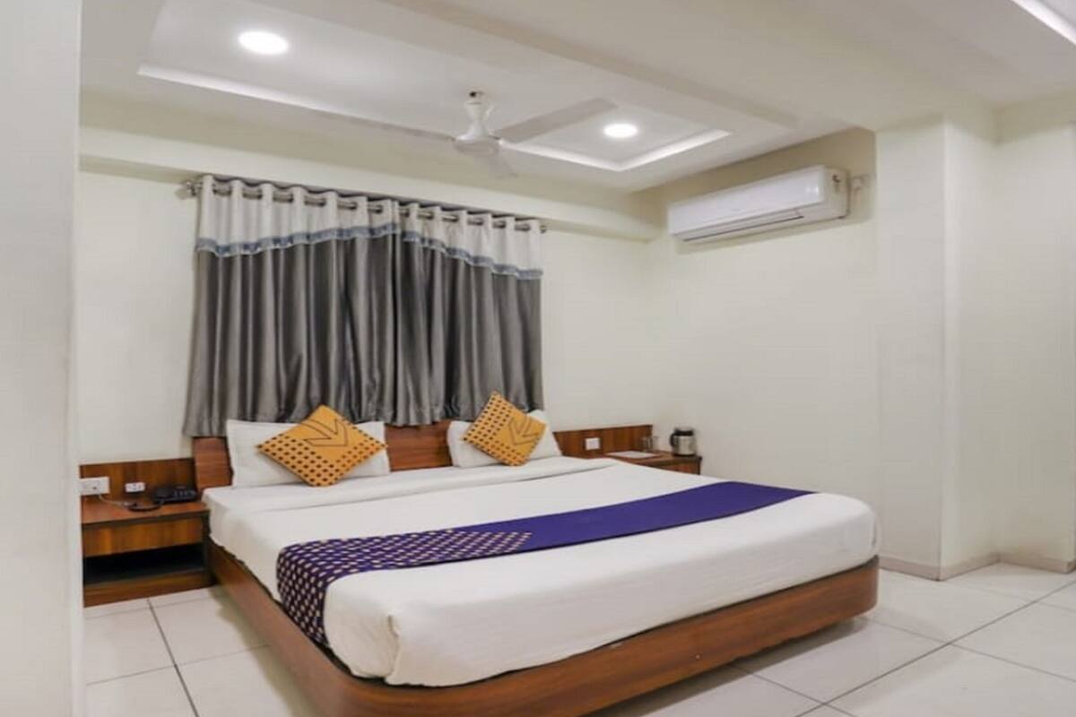 A bedroom with a large bed, wooden headboard, a bedside table, an air conditioning unit, and a door with a curtain.