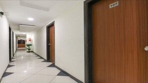 A corridor with a tiled floor, a wooden door with a number plate, and a small plant. - Everest Hotel  (Sanand)