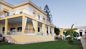 Un edificio de dos pisos con balcones, techo plano y un césped.