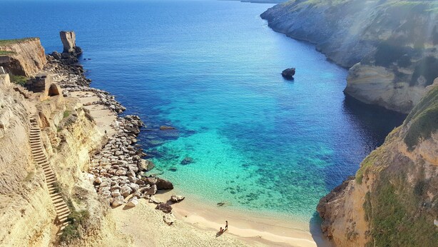 Un paisaje costero con mar azul turquesa, acantilados rocosos y una playa de arena.