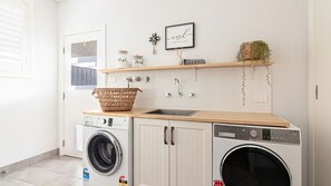 Une buanderie équipée d’un lave-linge, d’un sèche-linge, d’un évier et d’un panier posé sur le plan de travail.
