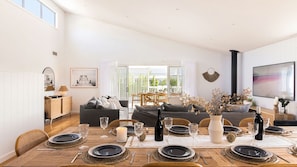 Un salon moderne avec un coin repas aménagé pour un repas, comprenant un canapé, une table à manger et une vue sur l’extérieur.
