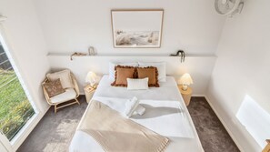 Une chambre à coucher comprenant un lit, deux tables de chevet, une chaise, une fenêtre et une œuvre d’art accrochée au mur.
