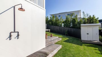A residential backyard with a white house, a wooden deck, a small shed, and a metal water feature.