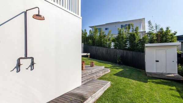 Ein Wohngrundstück mit einem weißen Haus, einer Holzterrasse, einem kleinen Schuppen und einem Wasserspiel aus Metall.
