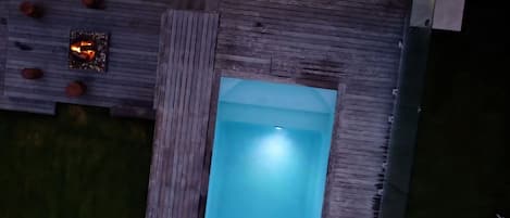 A rooftop pool with a wooden deck and string lights.