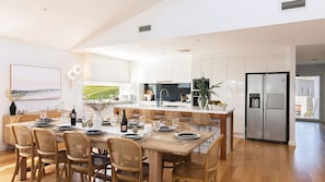 Une cuisine moderne avec des meubles blancs, un îlot central et un coin repas doté de meubles en bois.