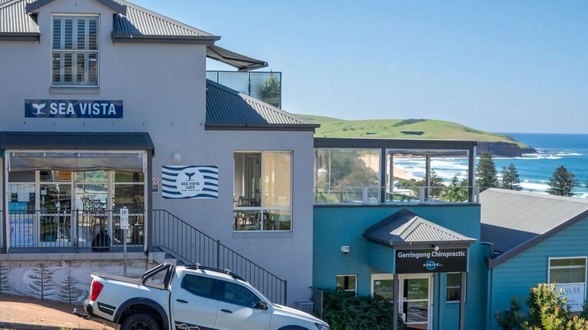 A coastal building with a cafe named 'Sea Vista Cafe' and a chiropractic clinic named 'Gerrington Chiropractic.'