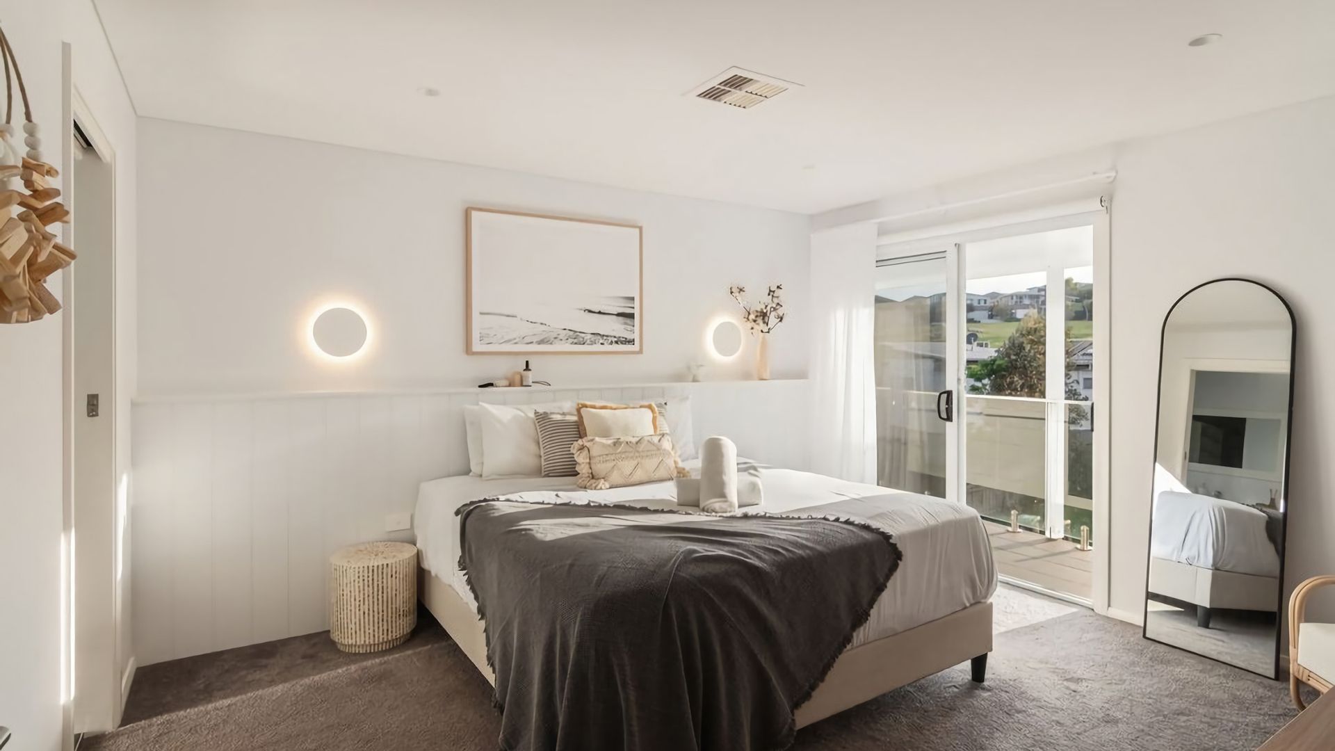 A bedroom with a bed, bedside lamps, a round mirror, and a view through a glass door.
