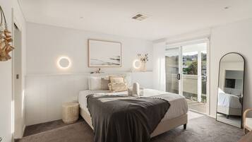 A bedroom with a bed, bedside lamps, a round mirror, and a view through a glass door.