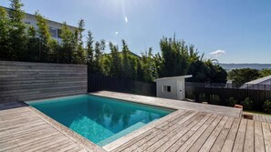 A swimming pool with a wooden deck, surrounded by a wooden fence and trees.