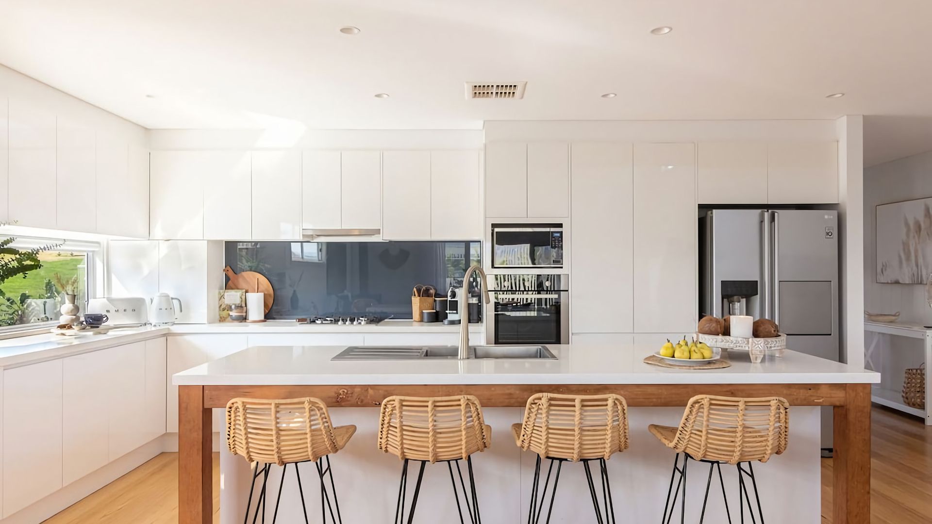 A modern kitchen with white cabinetry, a central island with bar stools, a built-in oven, and a refrigerator.