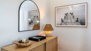 Ein Zimmer mit einem Holzkonsolentisch, einem Spiegel, einem gerahmten Foto und einer Lampe.