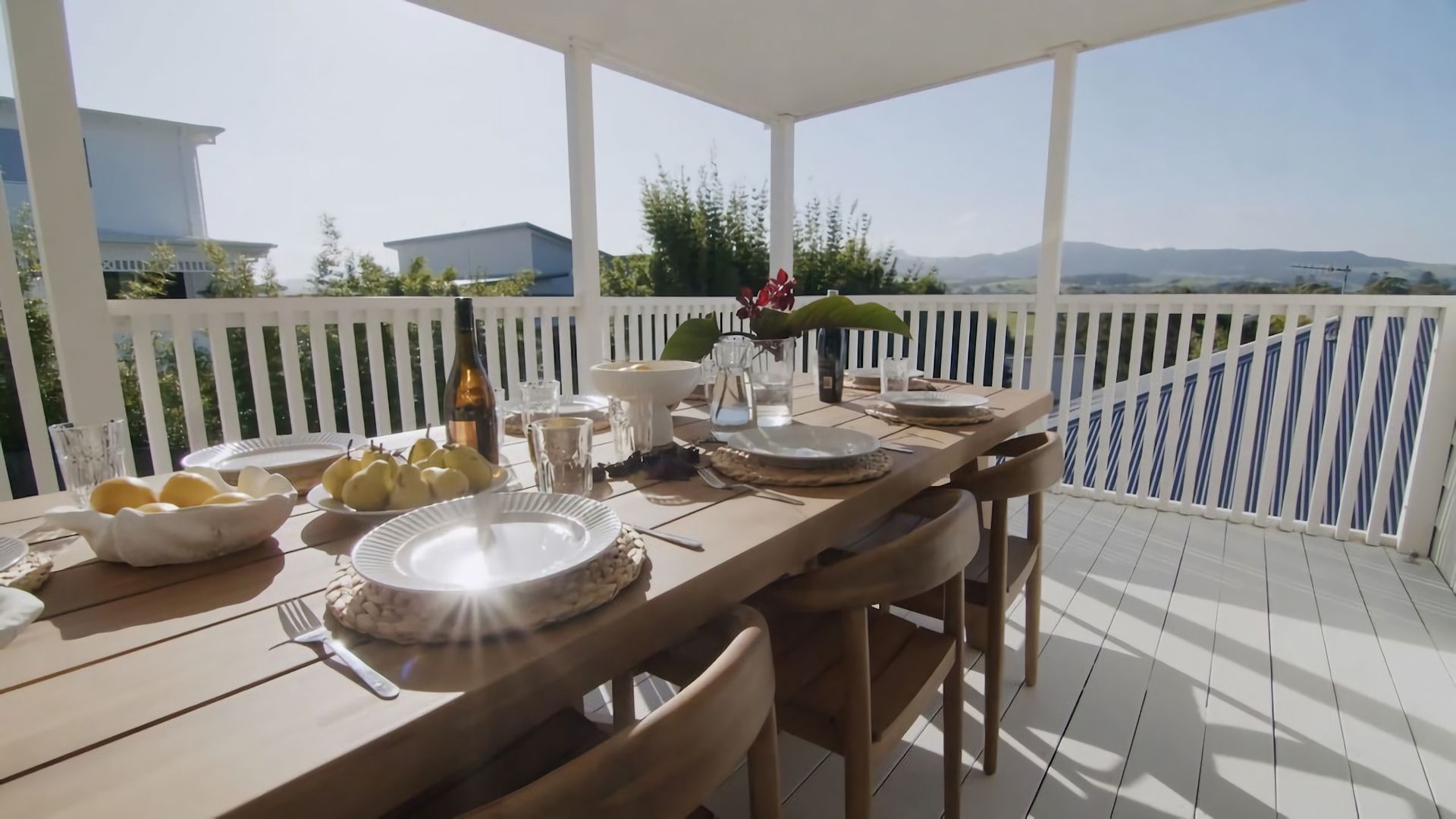 A covered outdoor dining area with a table set for four, surrounded by white railings, and overlooking a mountainous landscape.
