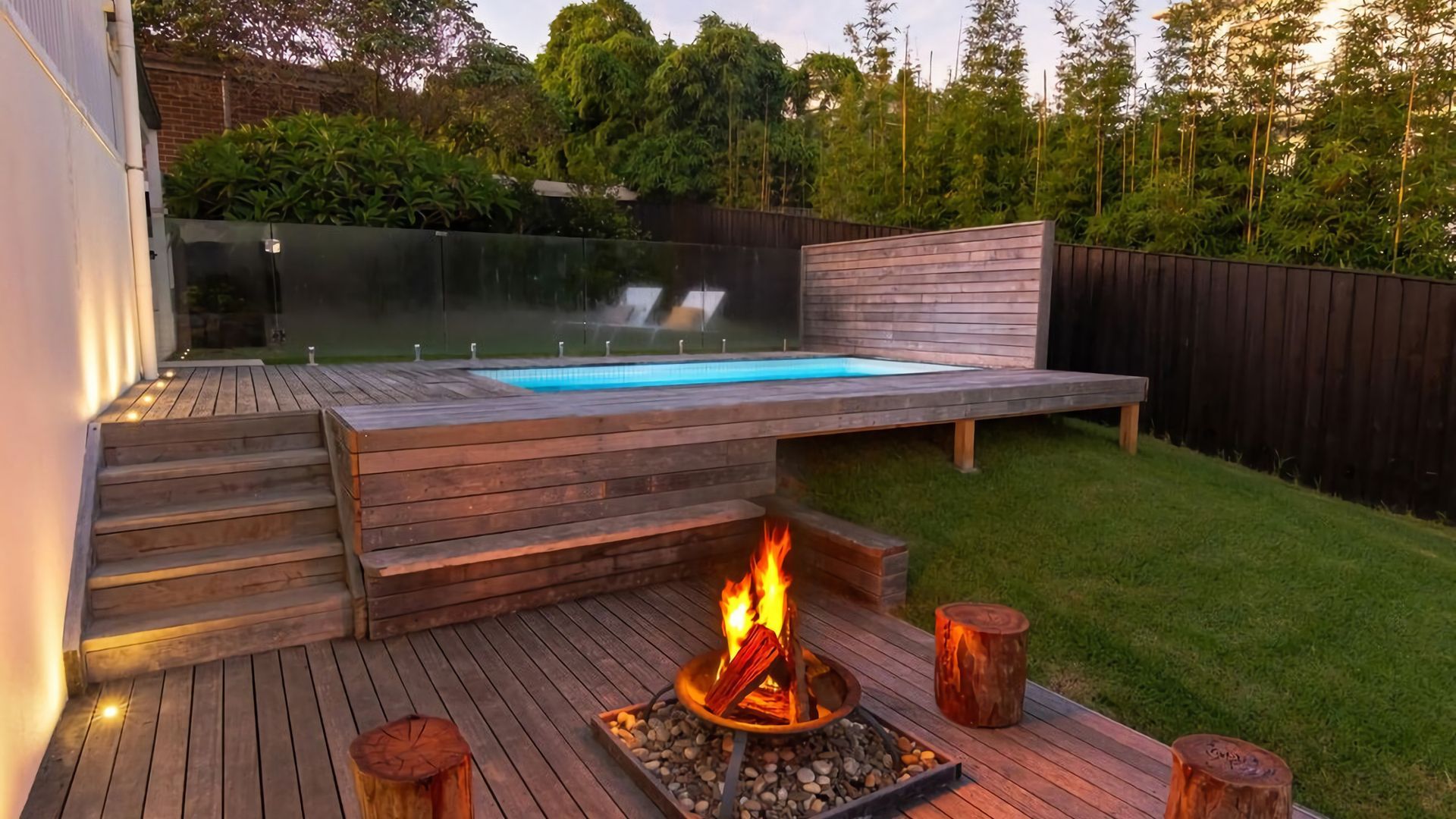 A backyard with a wooden deck, a fire pit, and a swimming pool.
