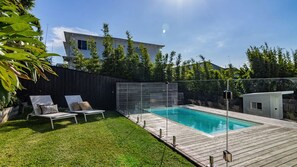 Un jardin avec une piscine, une terrasse en bois et une zone délimitée par une clôture.