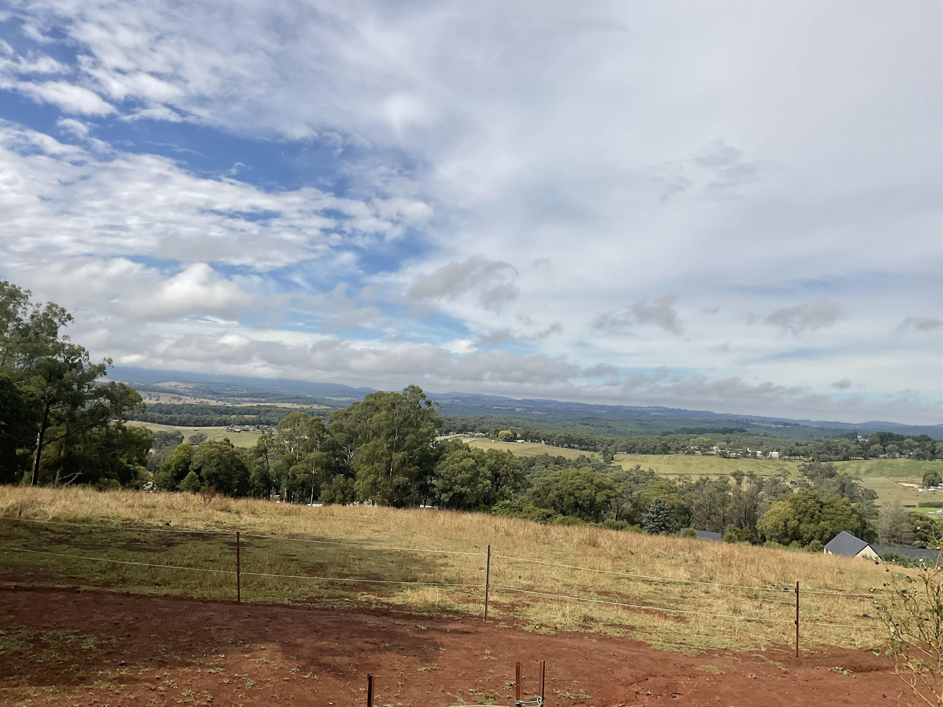 A rural landscape with a fence, trees, and distant hills.