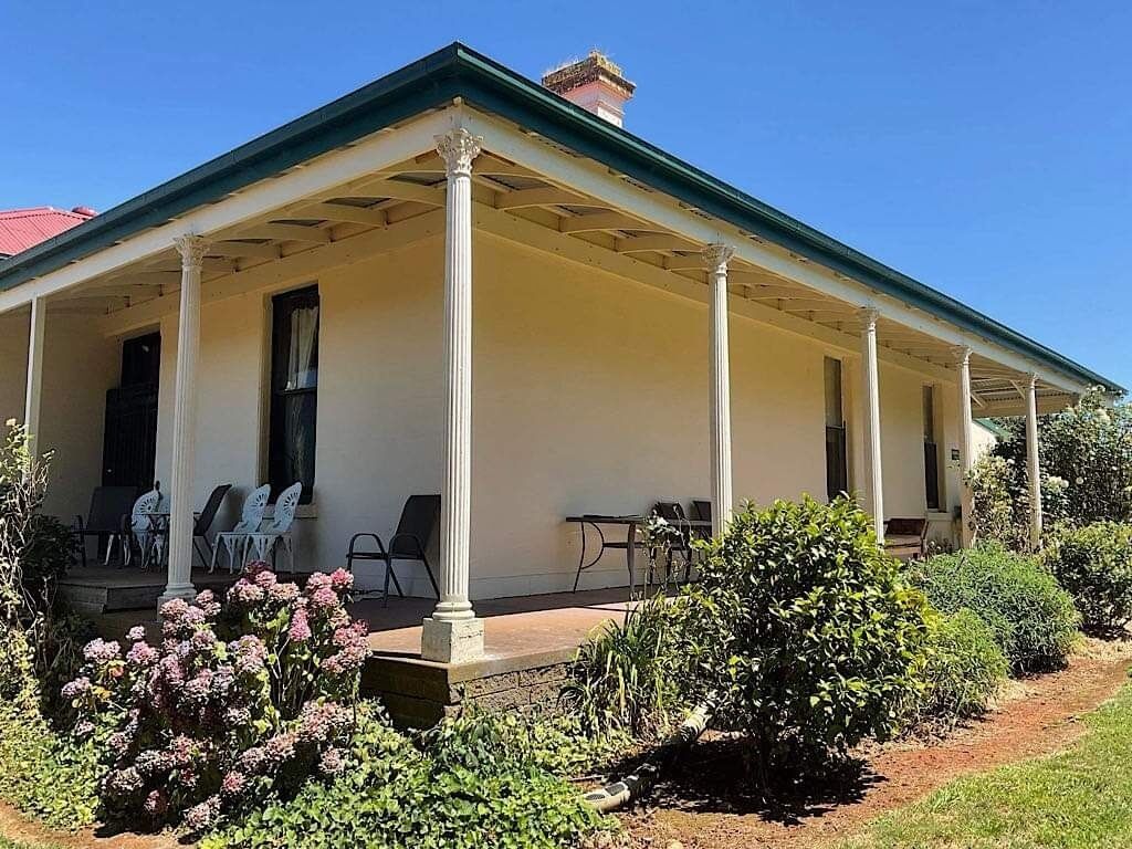 Una casa in stile coloniale su due piani, con un portico coperto, posti a sedere all'aperto e un giardino.