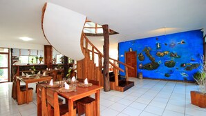 Restaurante com mobiliário de madeira, escada em espiral e parede azul decorada com ilustrações de peixes.