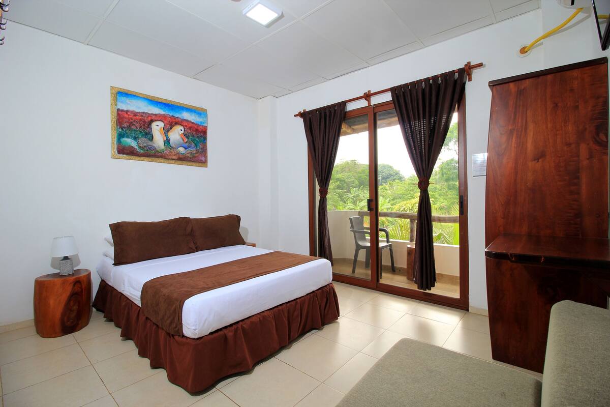A bedroom with a bed, a painting, a window with curtains, a chair, and a wooden cabinet.