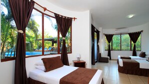 Quarto de hotel com cama, escrivaninha e vista para uma piscina e palmeiras.