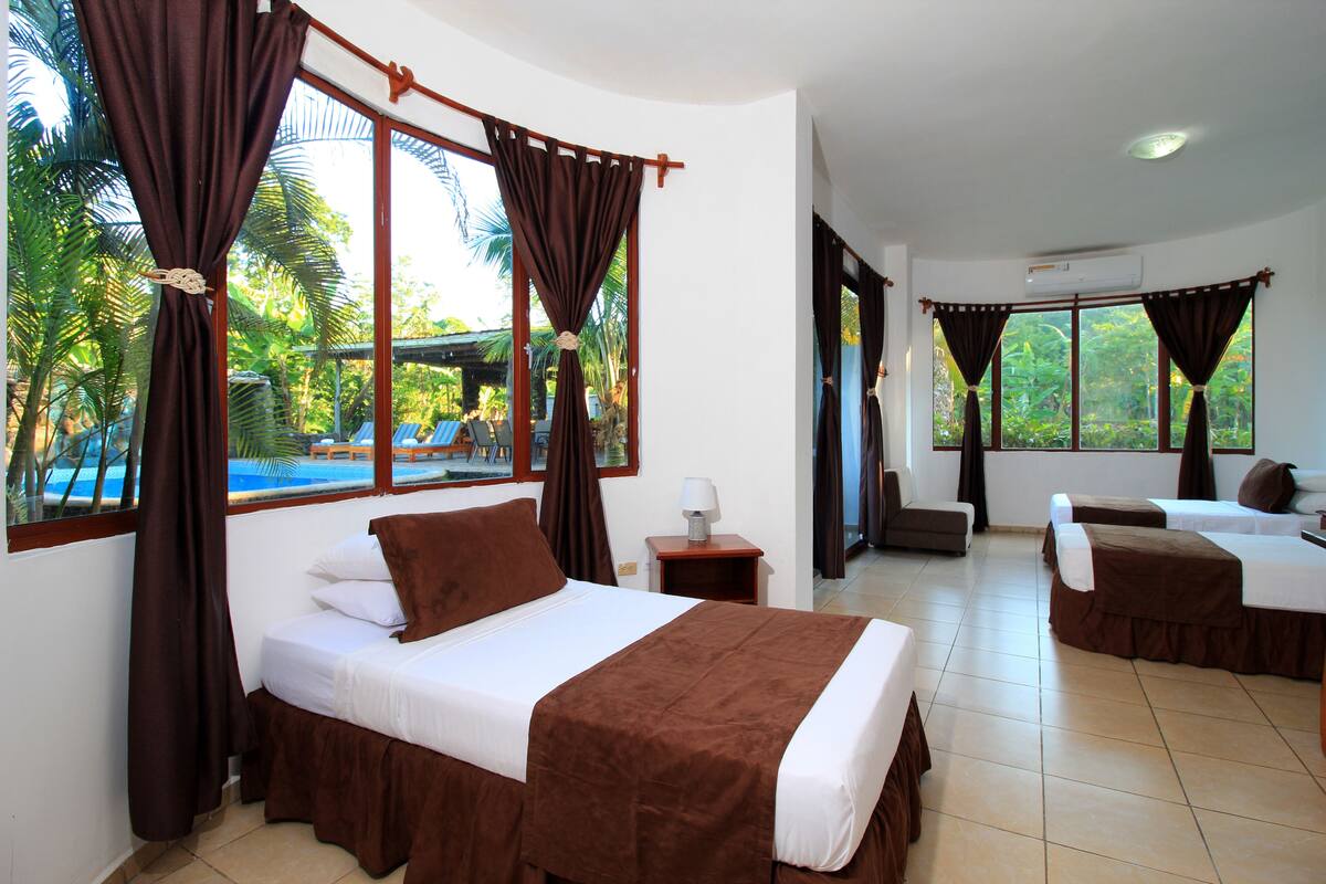 A hotel room with a bed, a desk, and a view of a pool and palm trees.