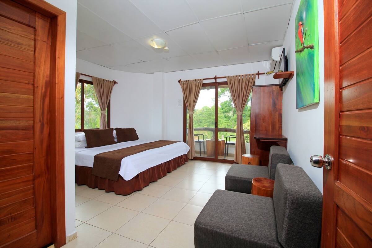 A hotel room with a bed, a sofa, a small table, and a painting on the wall.