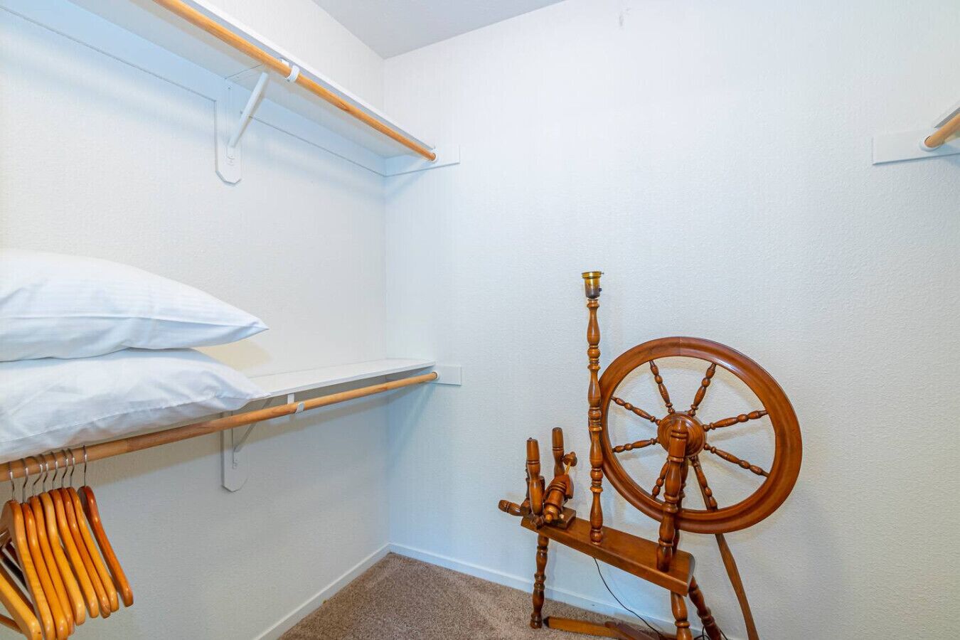 A small, neatly organized room with a bed, a shelf, and a spinning wheel.