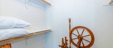 A small, neatly organized room with a bed, a shelf, and a spinning wheel.
