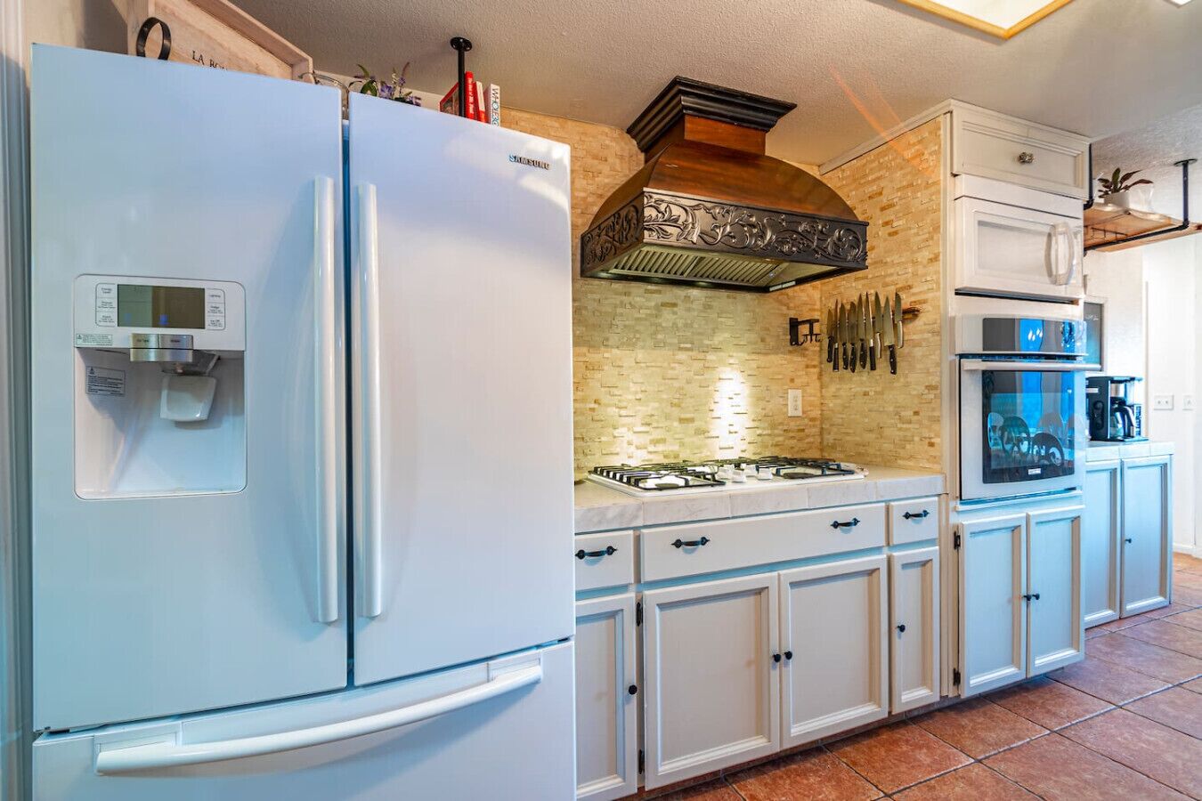 Een moderne keuken met een roestvrijstalen koelkast, een gasfornuis, witte kasten en een tegelwand van baksteen.