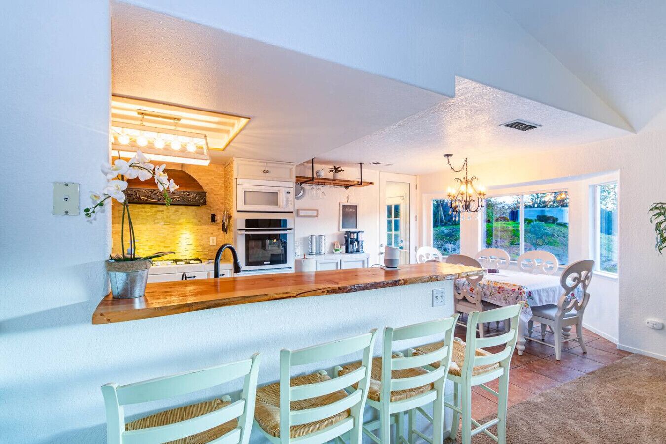 Una cocina moderna con una isla central, armarios blancos y un comedor con sillas de colores claros.