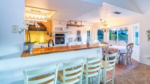 Una cocina moderna con una isla central, armarios blancos y un comedor con sillas de colores claros.