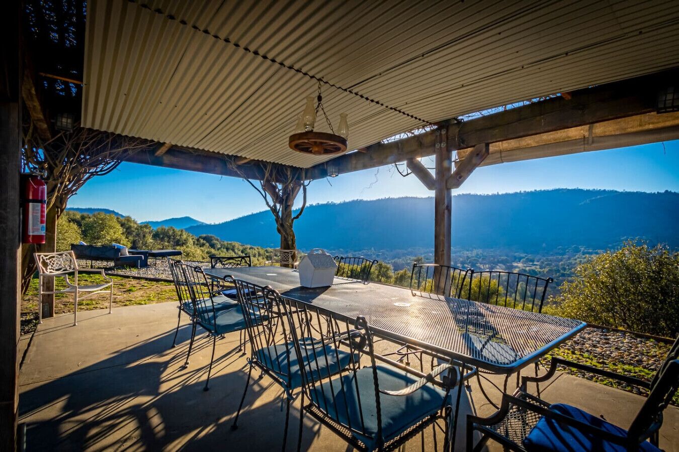 An outdoor dining area with a table and chairs, a hanging light fixture, and a view of mountains.