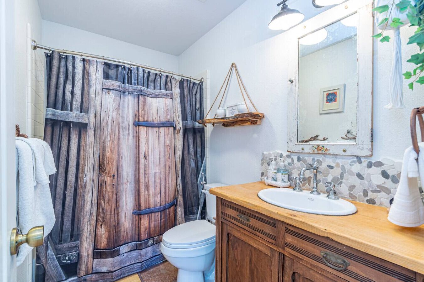 A bathroom with a rustic wooden shower curtain, a white toilet, a wooden vanity with a sink, and a mirror with a picture frame.